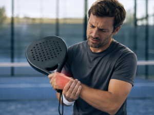 Jogador de padel segurando o punho com dor durante a prática do esporte, com destaque visual na região dolorida.